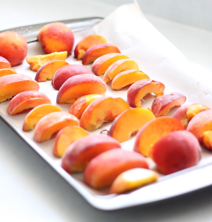 Sliced peaches on a baking sheet preparing for the freezer