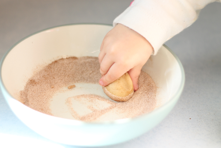 Child's hand rolling snickerdoodles in cinnamon & sugar