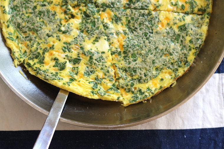 overhead shot of a spinach frittata in a pan with a serving utensil
