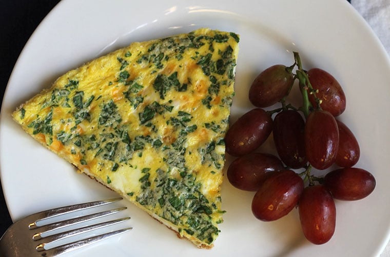 a slice of spinach frittata on a plate with grapes