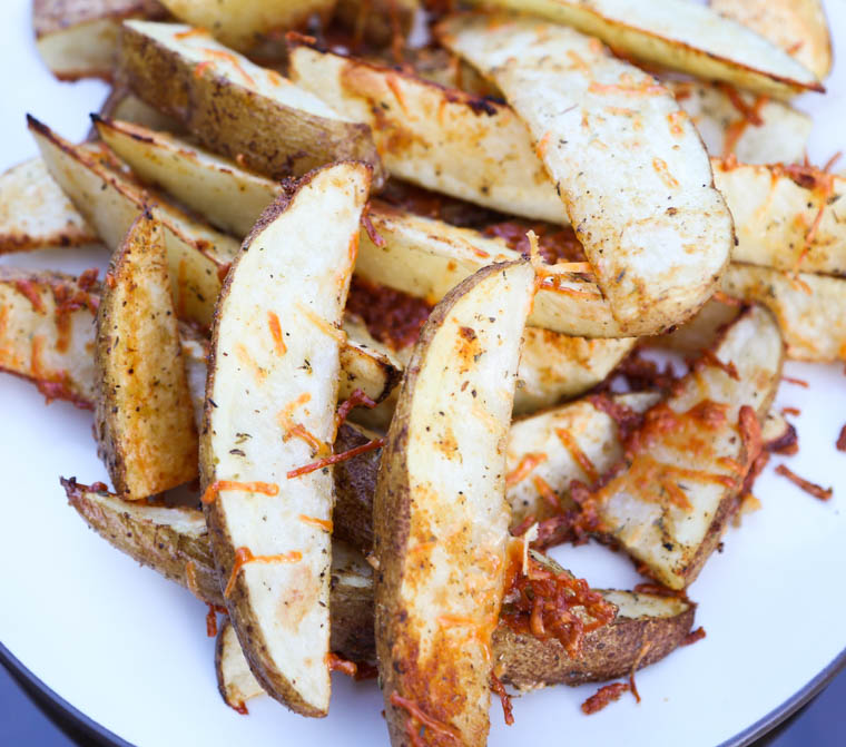 Crispy parmesan potato wedges cooked and stacked on a plate. 