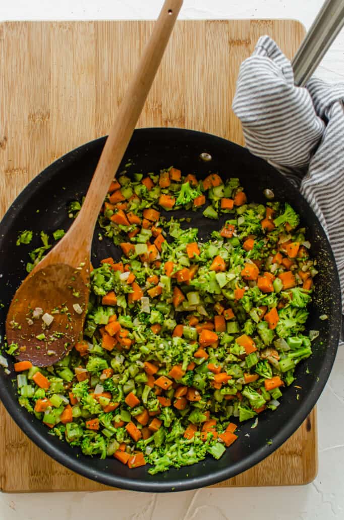 carrots, onions, and broccoli being sautéed in a cast iron pan