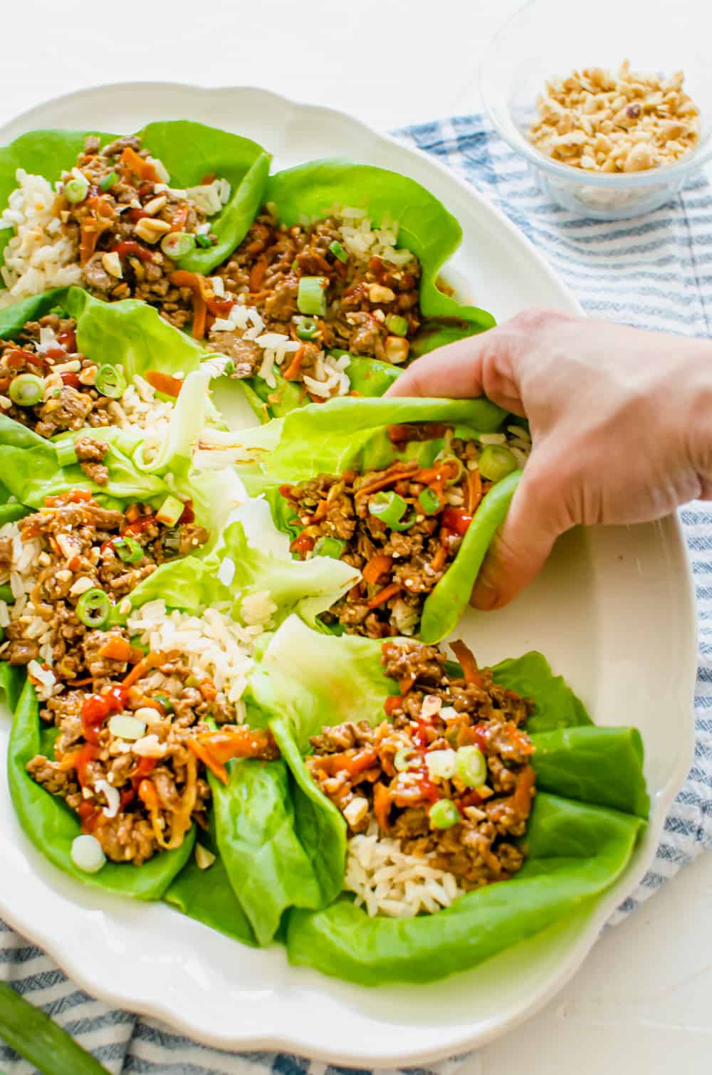 Chicken lettuce wraps on a platter with a hand grabbing one.