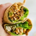 A hand holding two halves of an Asian Chicken wrap.