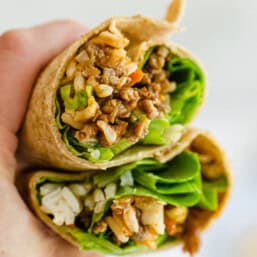A hand holding two halves of an Asian Chicken wrap.