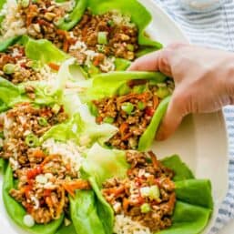 prepared chicken lettuce wraps on a platter with a hand grabbing one