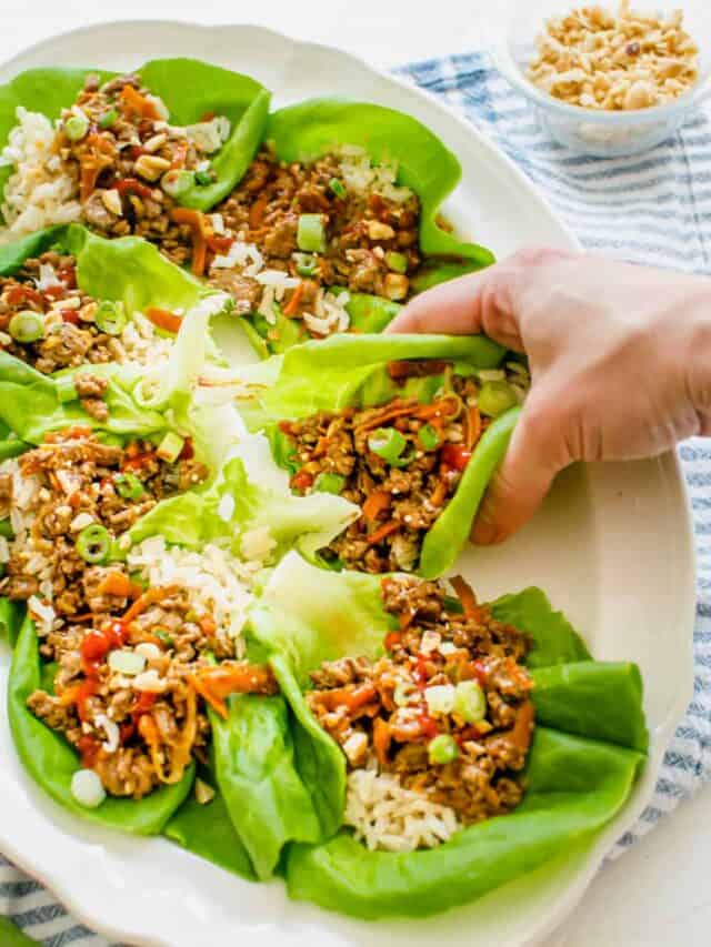 prepared chicken lettuce wraps on a platter with a hand grabbing one