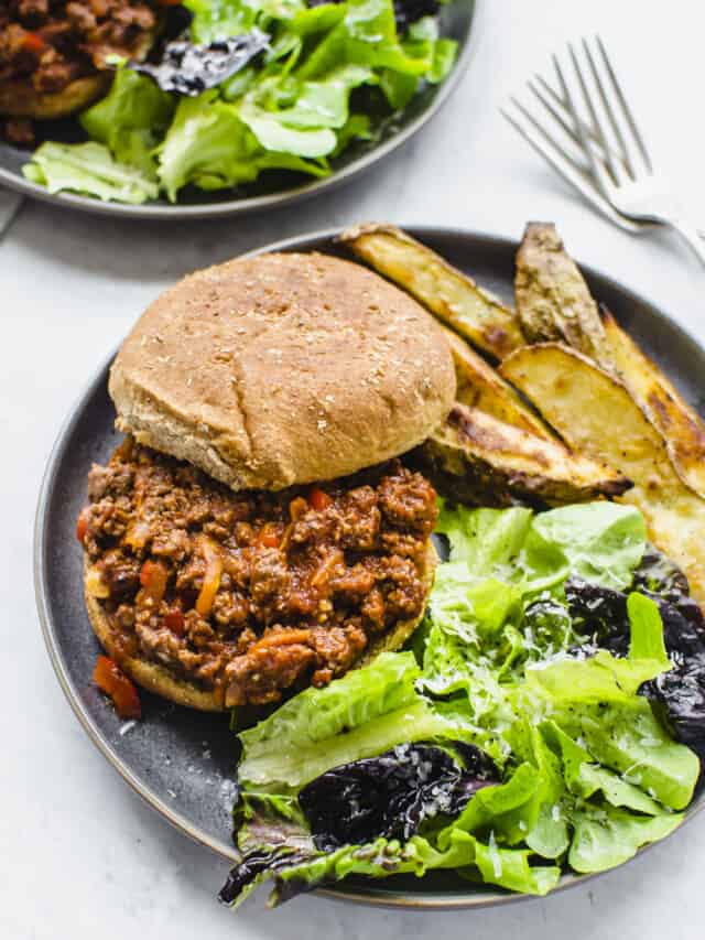 Sloppy joe recipe shown on wheat hamburger buns on a plate with salad and steak fries