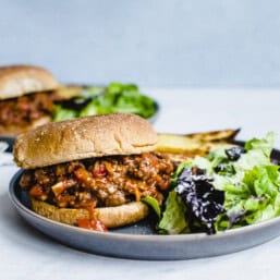 A homemade sloppy joe sandwich on a plate with salad.