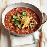 Vegetarian Tortilla Soup in a bowl with sliced jalepenos, fresh cilantro, and shredded cheddar cheese on top.