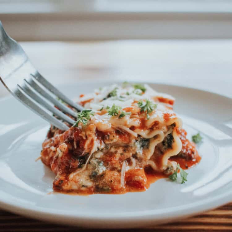 A spinach lasagna roll on a white plate with a fork.