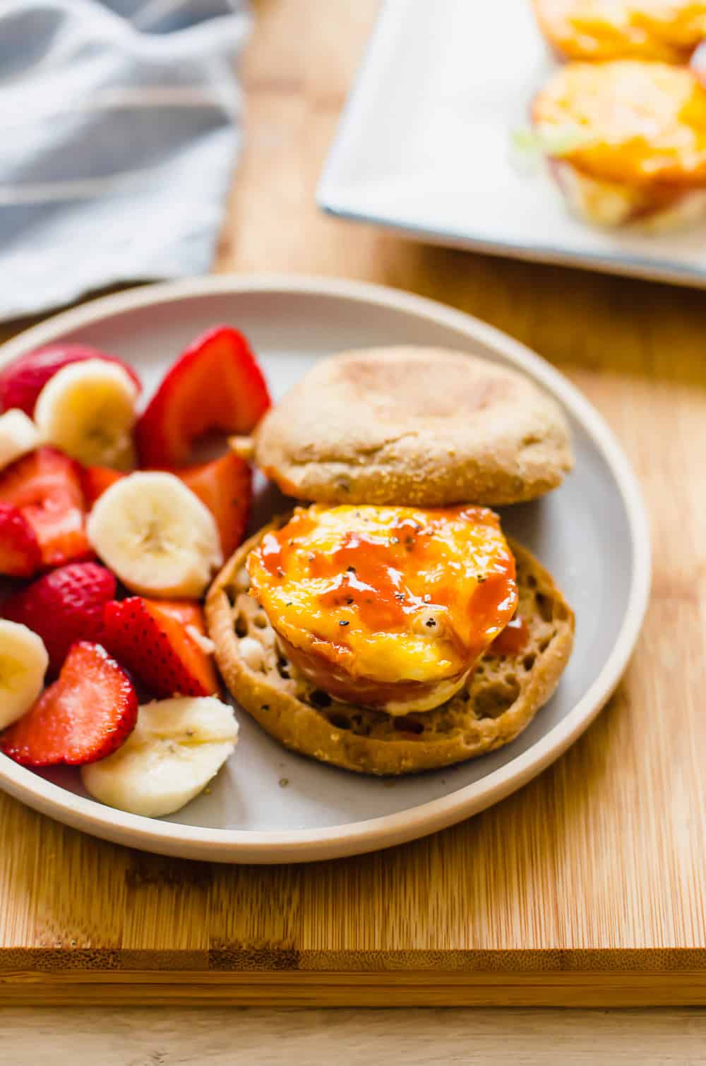 Ham and cheese egg cup on a toasted English muffin with hot sauce on top and fruit salad on the side.