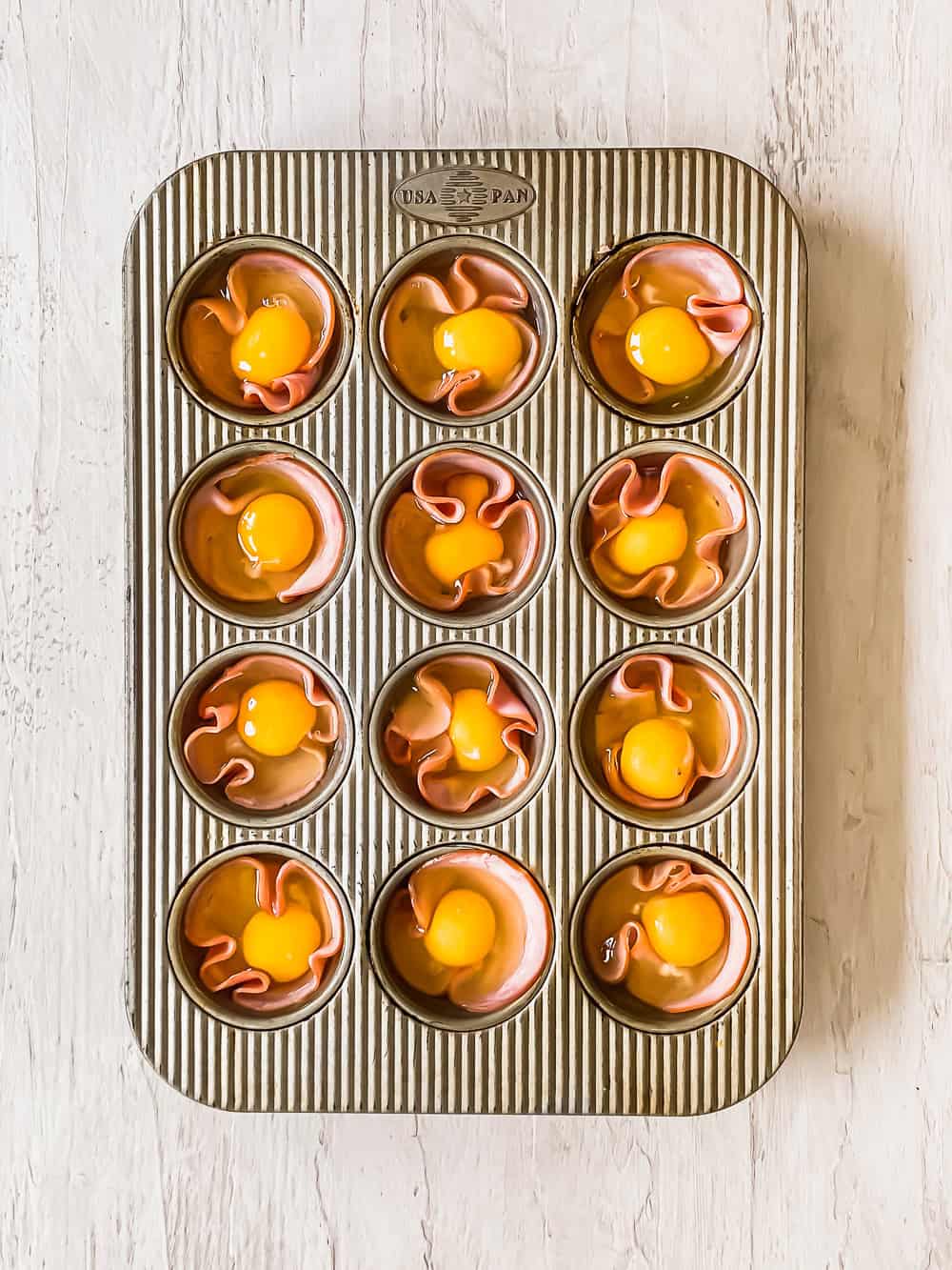 Ham slices and raw eggs in individual muffin cups.