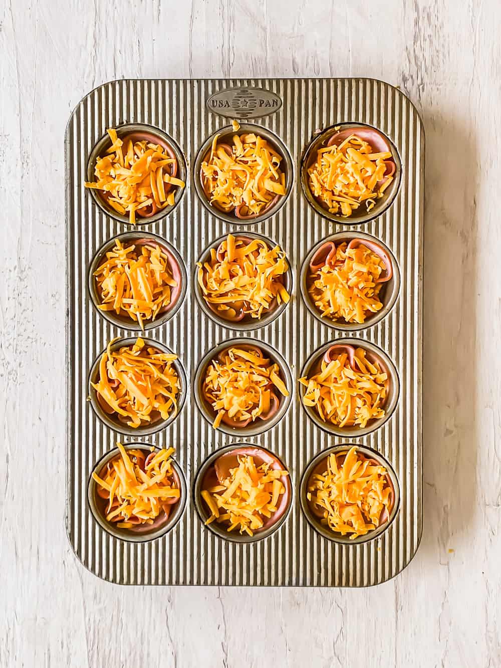 Ham, raw egg, and shredded cheddar cheese in individual muffin tins.