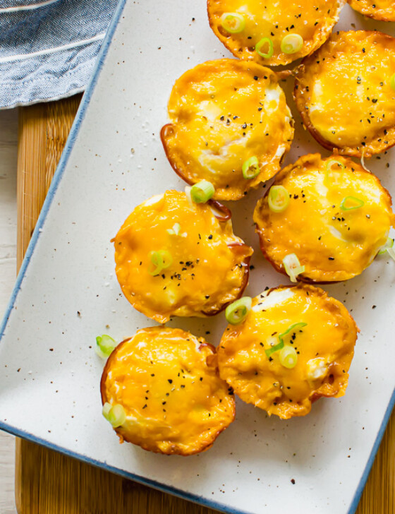 ham and cheese egg cups on a white serving platter with sliced green onions on top