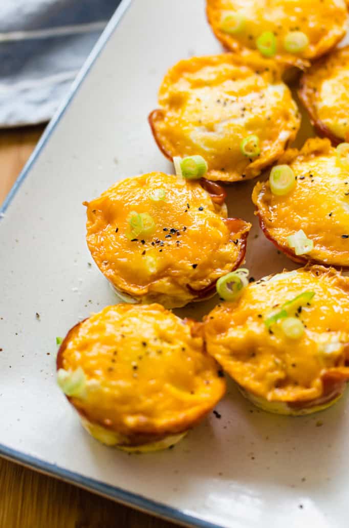 ham and cheese egg cups on a white serving platter with sliced green onions on top