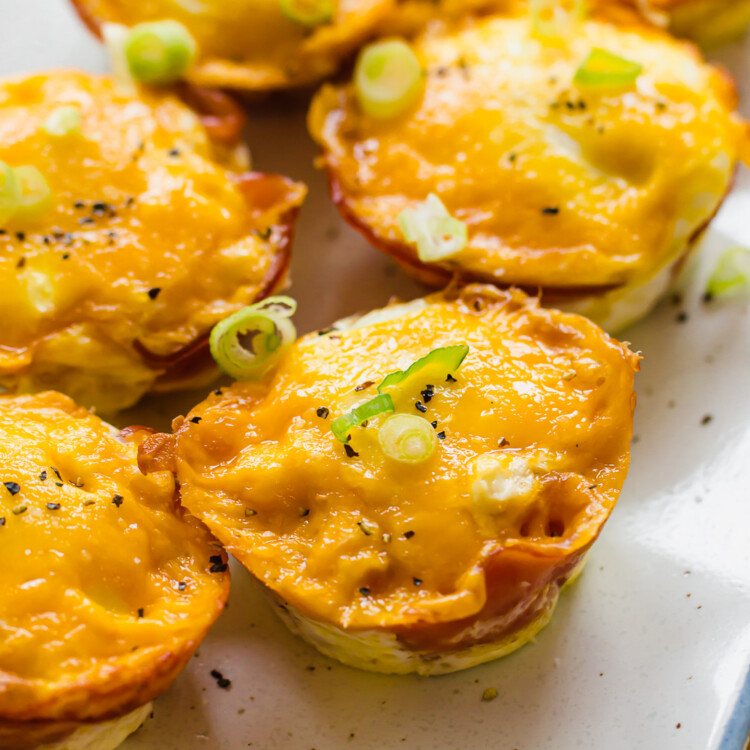 ham and cheese egg cups on a white serving platter with sliced green onions on top