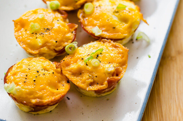 Ham and cheese egg cups on a white serving platter with sliced green onions on top.