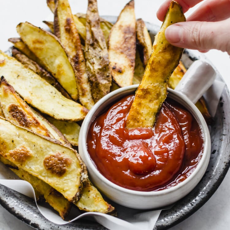 Oven-baked steak fries being dipped in ketchup.