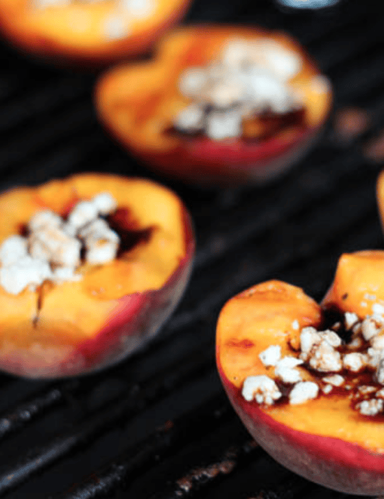 Grilled peaches still on the grill with Gorgonzola cheese in the middle of them.