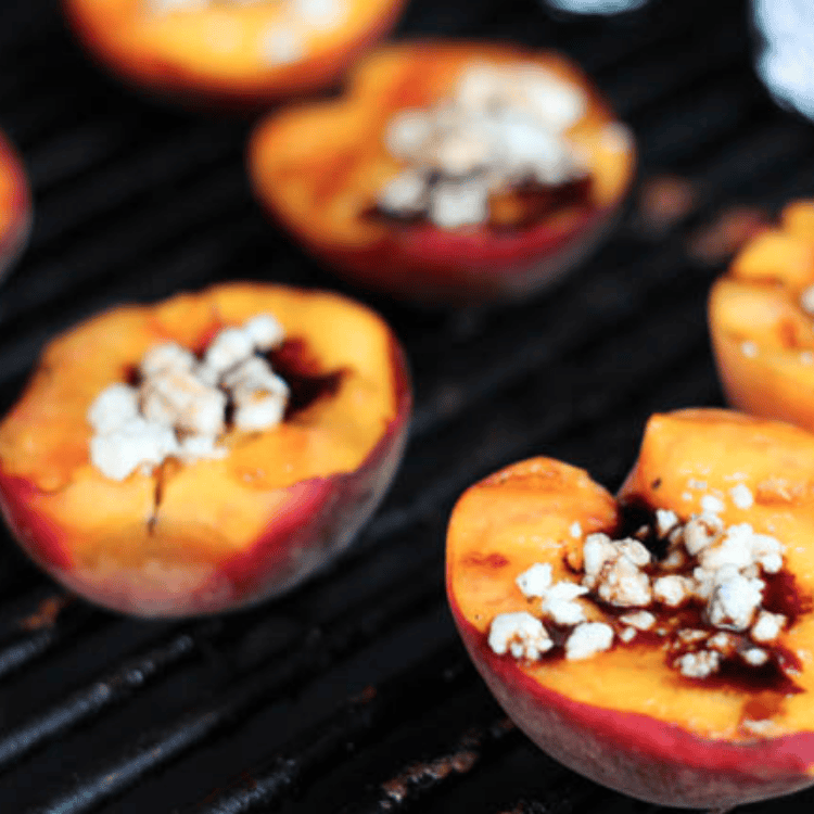 Grilled peaches still on the grill with Gorgonzola cheese in the middle of them.