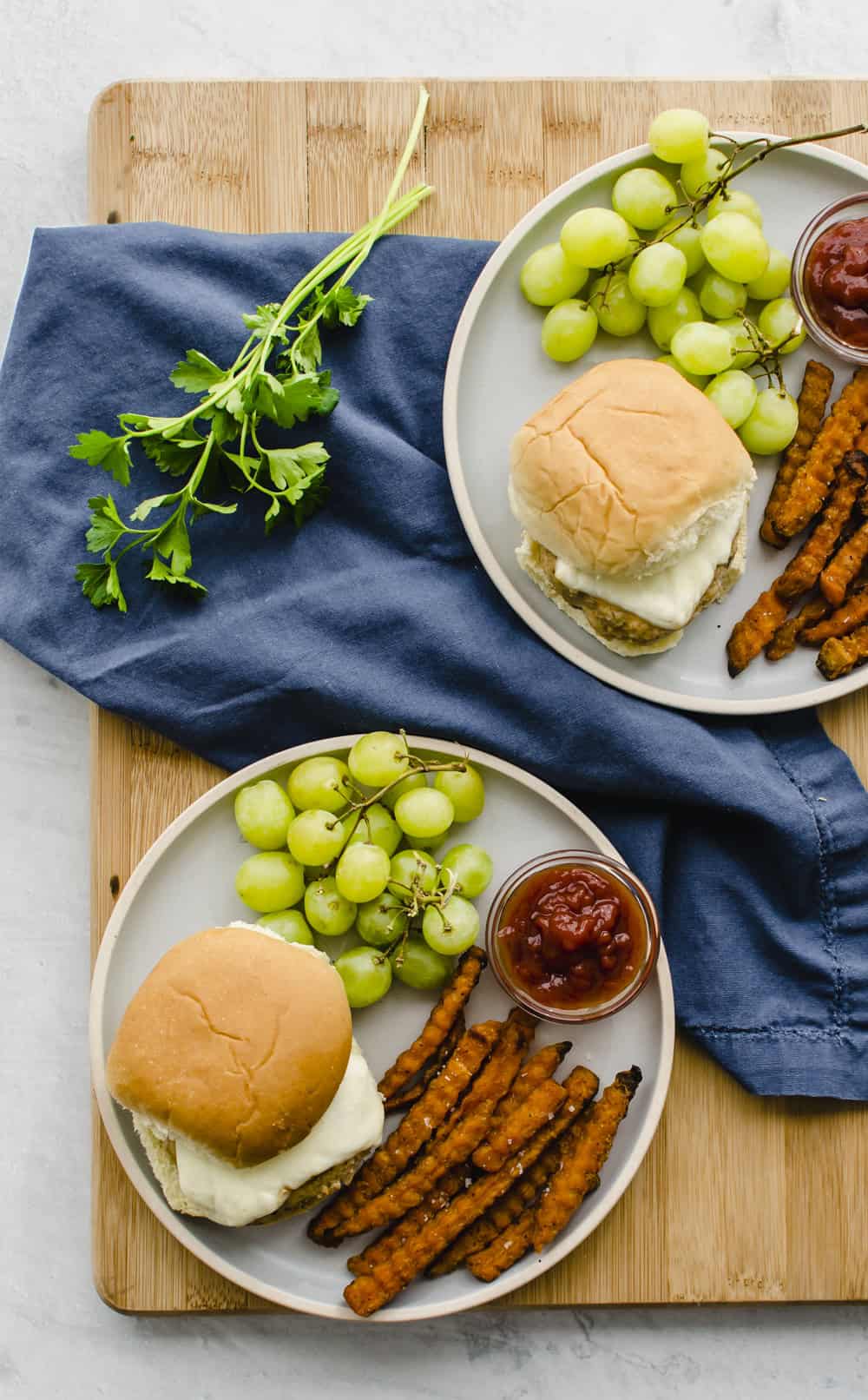 White plate with chicken burger on bun, sweet potato fries, and grapes.