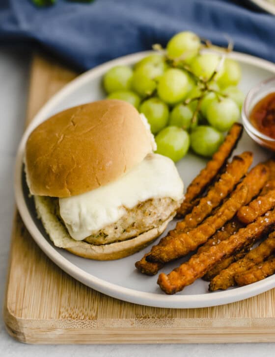 Mini chicken burger on a plate with grapes and sweet potato fries.