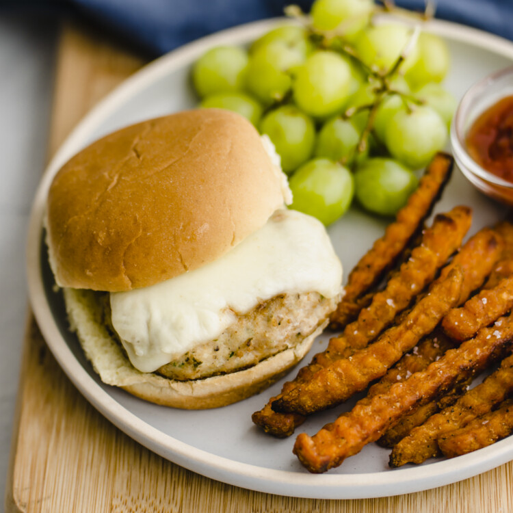 Mini chicken burger on a plate with grapes and sweet potato fries.