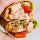 A hand holding southwest chicken wraps with sauce dripping out.