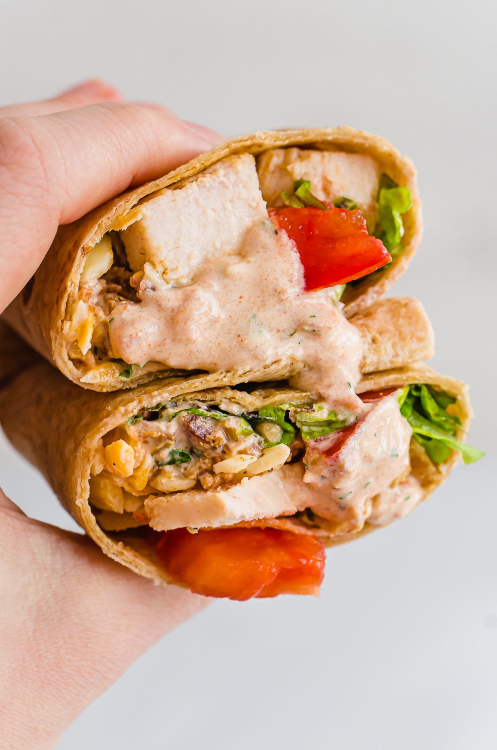 A hand holding two halves of a southwest chicken wrap stacked together with creamy southwest ranch dressing.