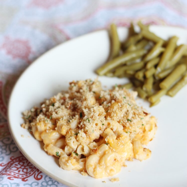 Healthy mac and cheese served on a white plate with green beans on the side.