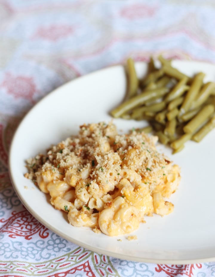 Healthy mac and cheese served on a white plate with green beans on the side.