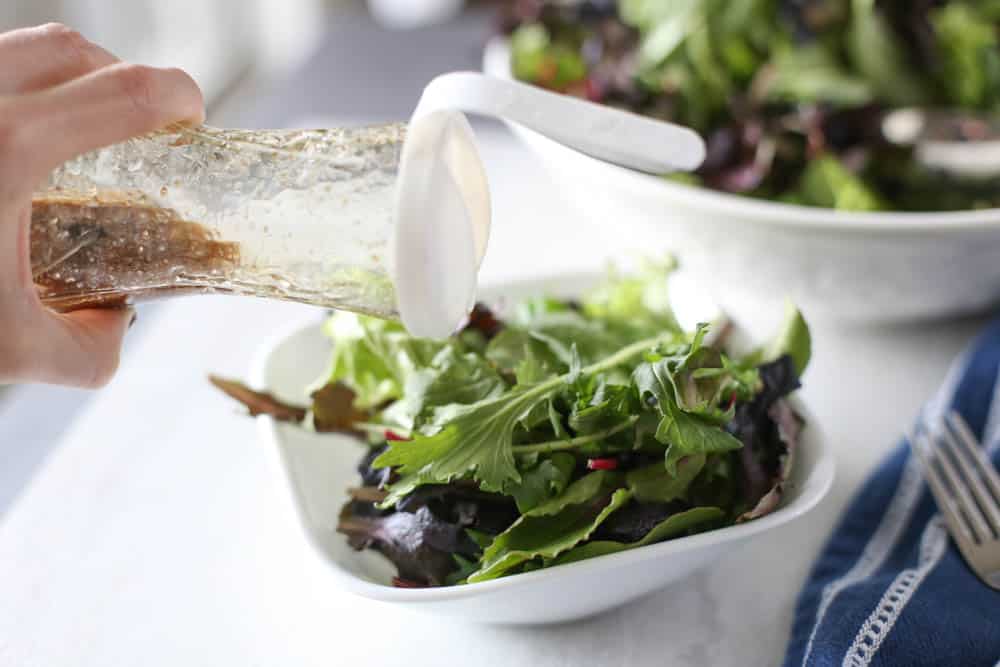 Bowl of lettuce with dressing being poured on top.