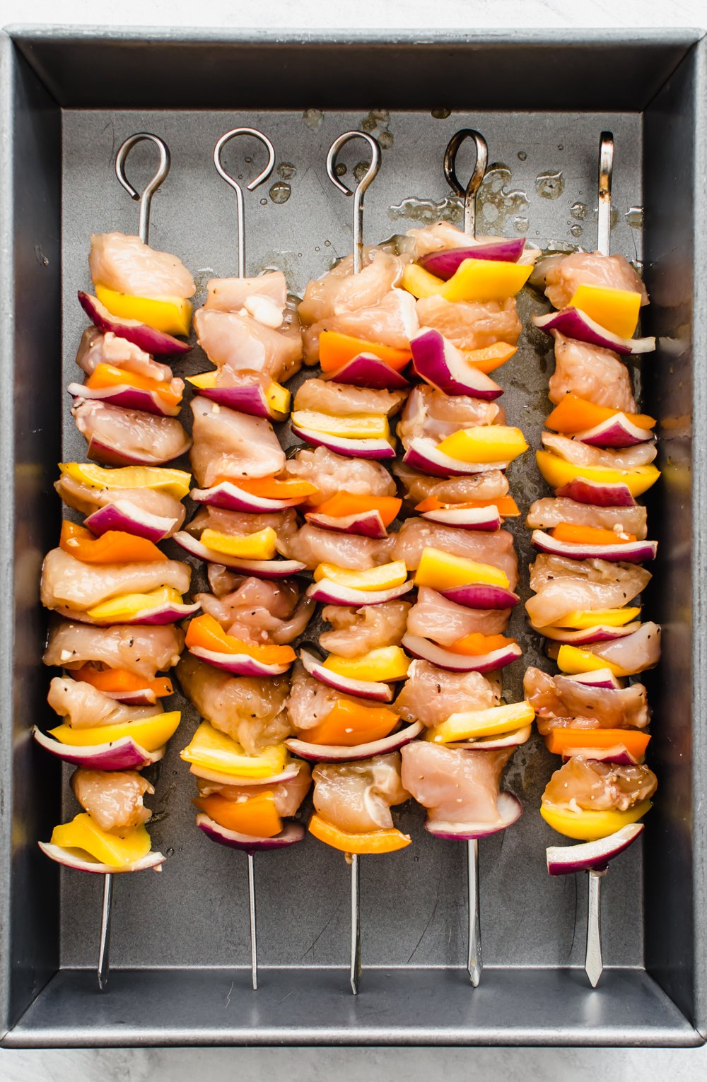 Raw chicken and veggies on skewers in a pan ready for the grill.