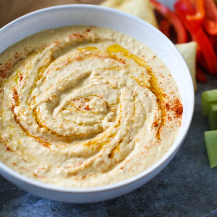 Homemade hummus in a white bowl with raw veggies on the side.