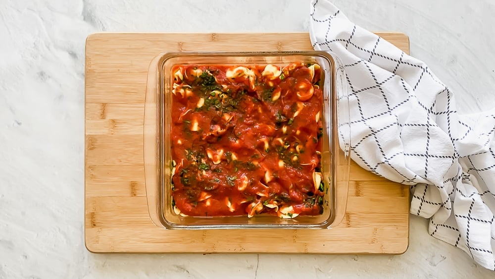 An 8x8 dish with layers of marinara sauce, cheese tortellini, spinach, and more marinara sauce.