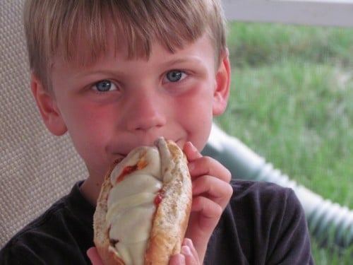 A small boy smiling while holding a meatball sub.