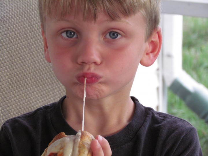 A small boy taking a bite of meatball sub sandwich.