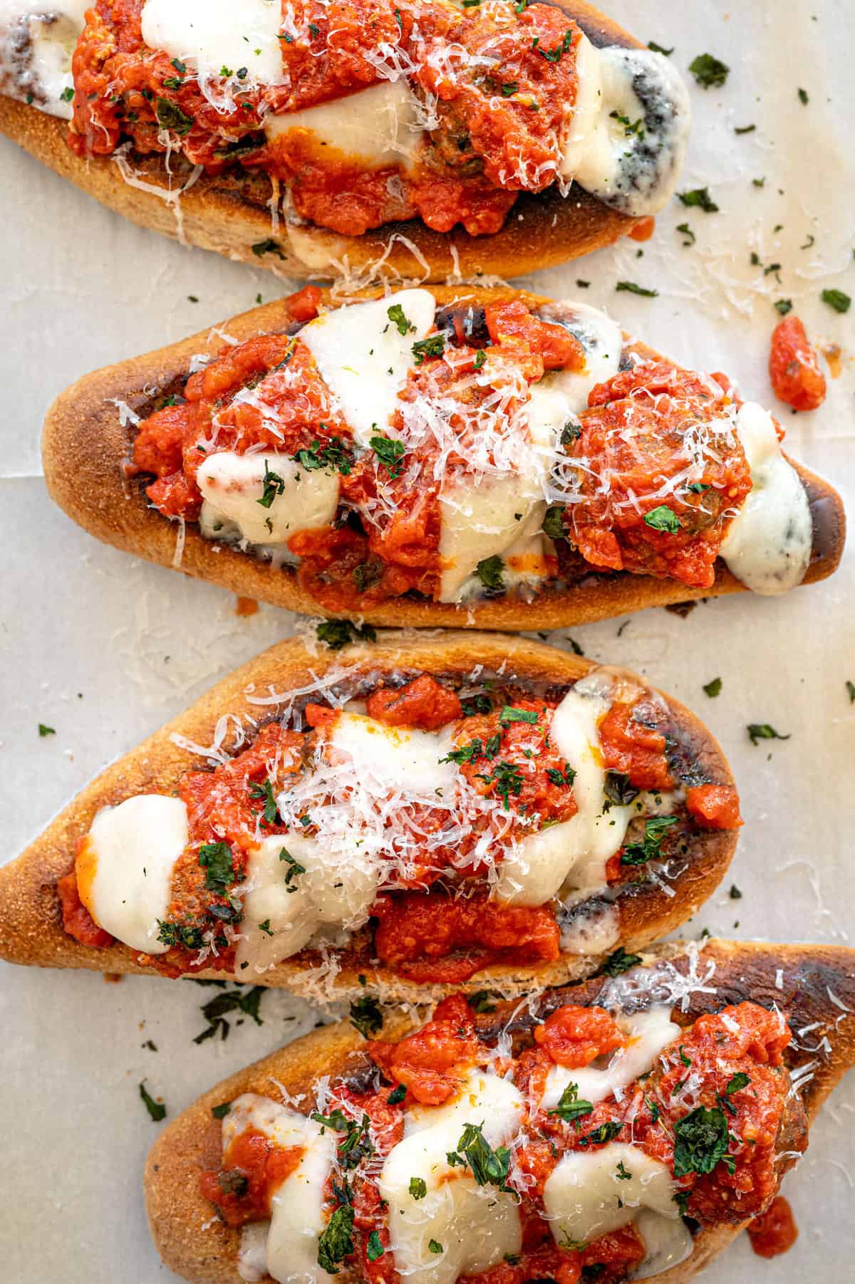 Meatball subs lined up on parchment paper with fresh parsley sprinkled over the tops.