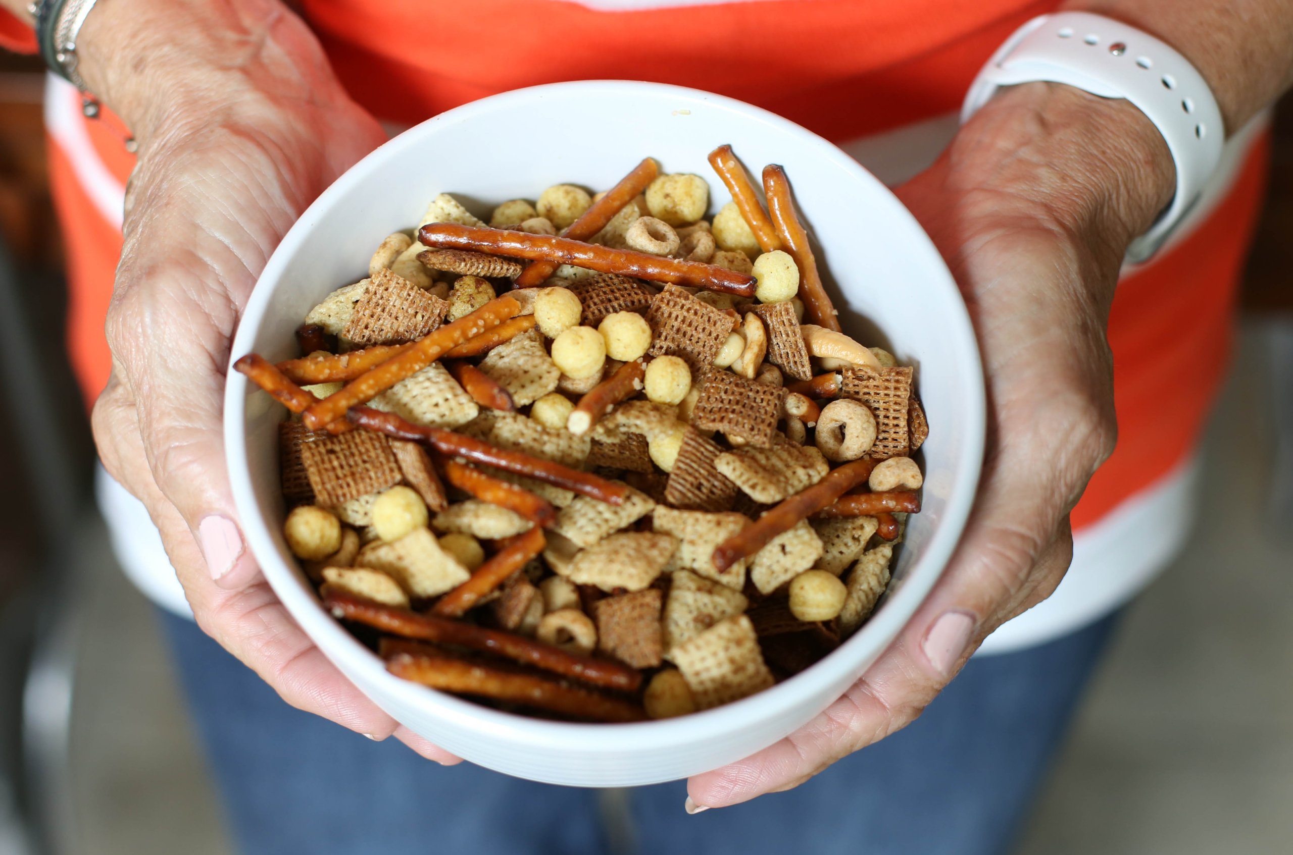 Hands holding a small white bowl of Homemade Chex Mix.
