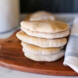 Whole wheat homemade pita bread stacked up on a cutting board.