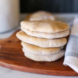 Whole wheat homemade pita bread stacked up on a cutting board.