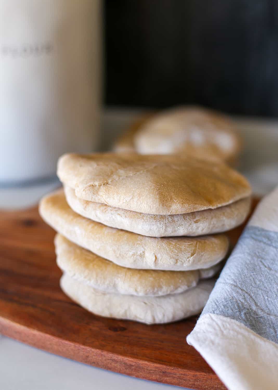 A stack of whole wheat pita bread on a wooden cutting board.