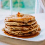 A stack of zucchini pancakes with maple syrup being poured on top.