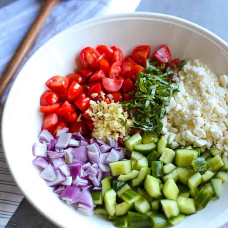 chopped cucumber, red onion, tomatoes, basil, garlic and crumbled feta in a white bowl