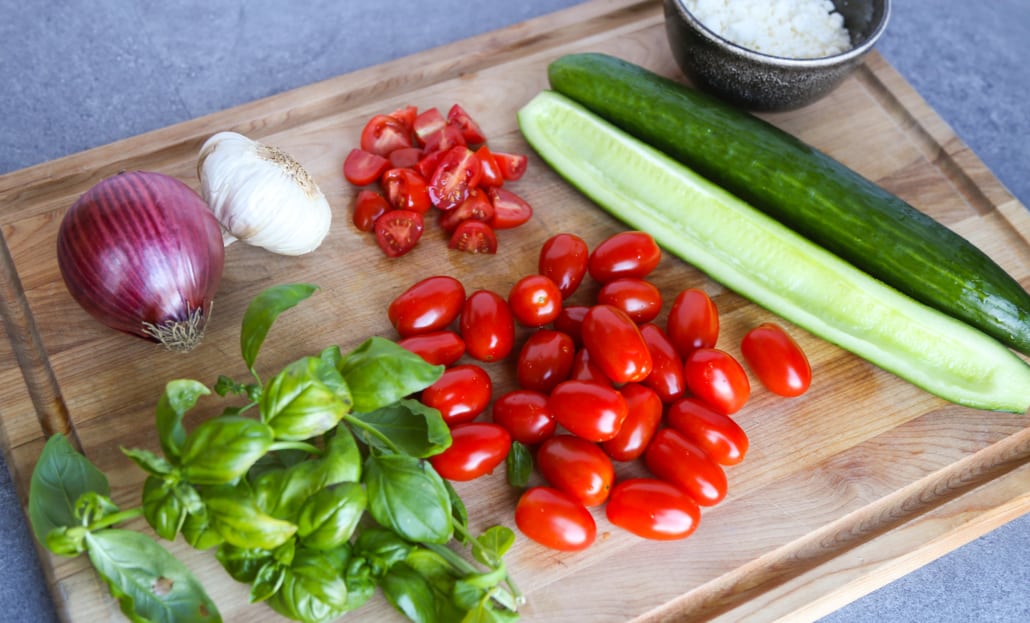 cucumber, cherry tomatoes, basil, garlic, and red onion on a wooden cutting board
