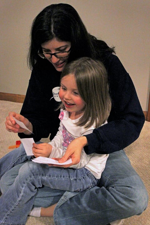 Adult holding child in her lap and looking at the Apples to Apples game pieces of paper.