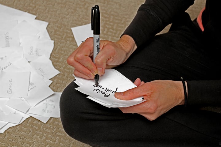 Woman writing on pieces of paper with a marker for Apples to Apples game.