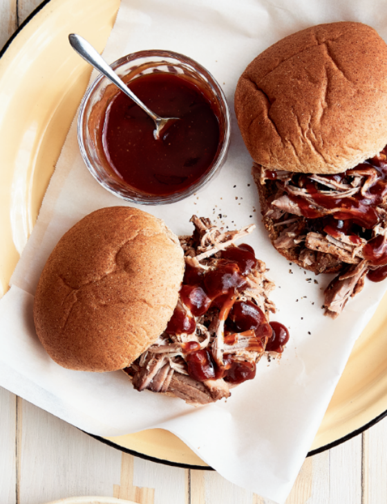 Two pulled pork sandwiches on a plate with a small bowl of BBQ sauce on it as well.