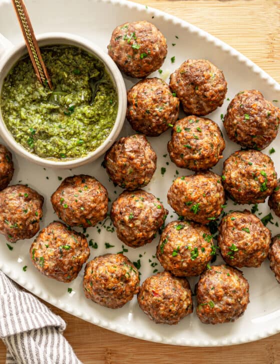 baked healthy meatballs on a platter with pesto in a small bowl